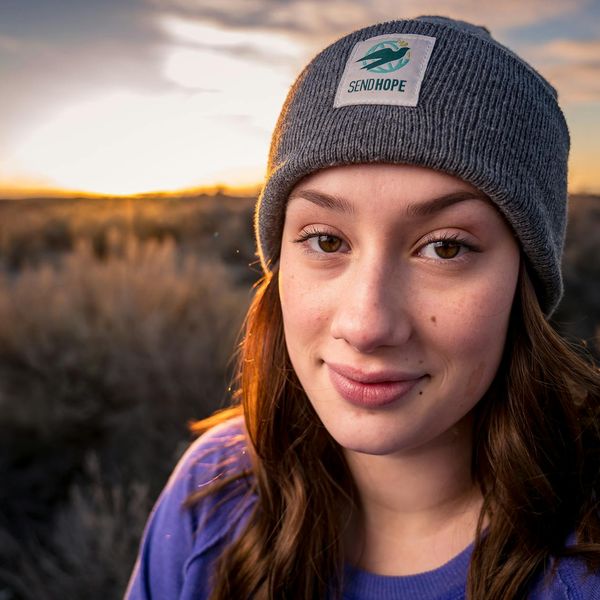 Person smiling peacefully with eyes closed in a calm, natural setting.